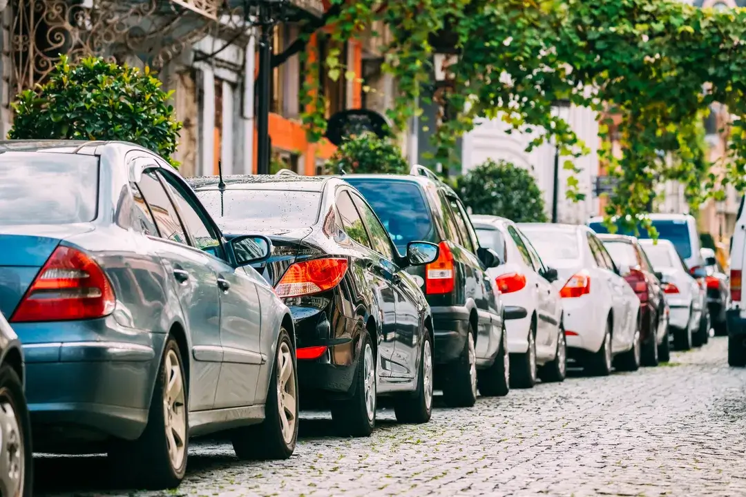 Many cars parked on street in city in sunny summer